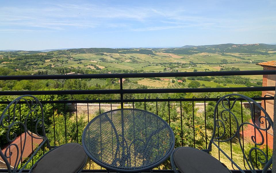 Vista panoramica su colline verdi da un terrazzo con tavolo e sedie eleganti.