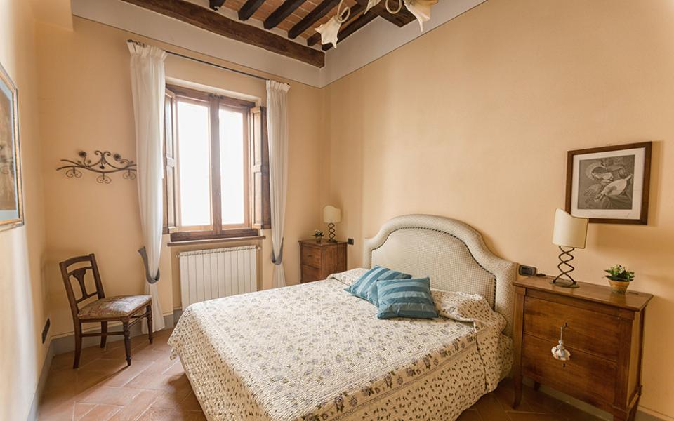 Camera da letto accogliente con mobili in legno e dettagli classici, illuminata da una finestra.