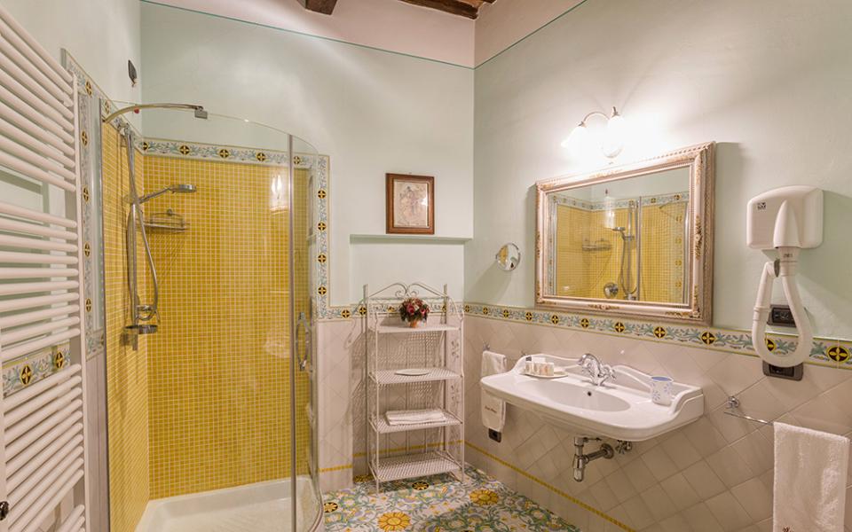 Bagno luminoso con doccia, piastrelle colorate e specchio incorniciato.