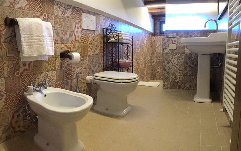 Bagno con piastrelle colorate, bidet, WC, lavabo e portasciugamani.