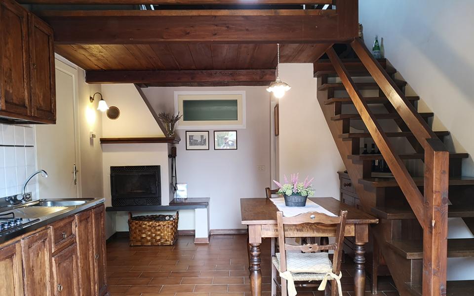 Cucina rustica con tavolo in legno, camino e scala in legno.