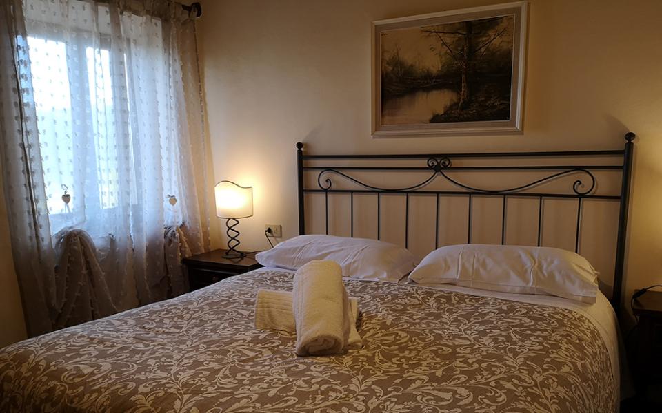 Camera accogliente con letto matrimoniale, lampada e asciugamani su copriletto decorato.