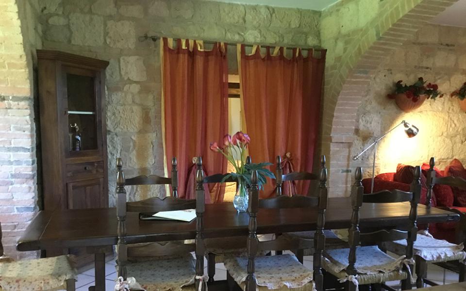 Sala da pranzo rustica con tavolo in legno, sedie imbottite e fiori sul tavolo.