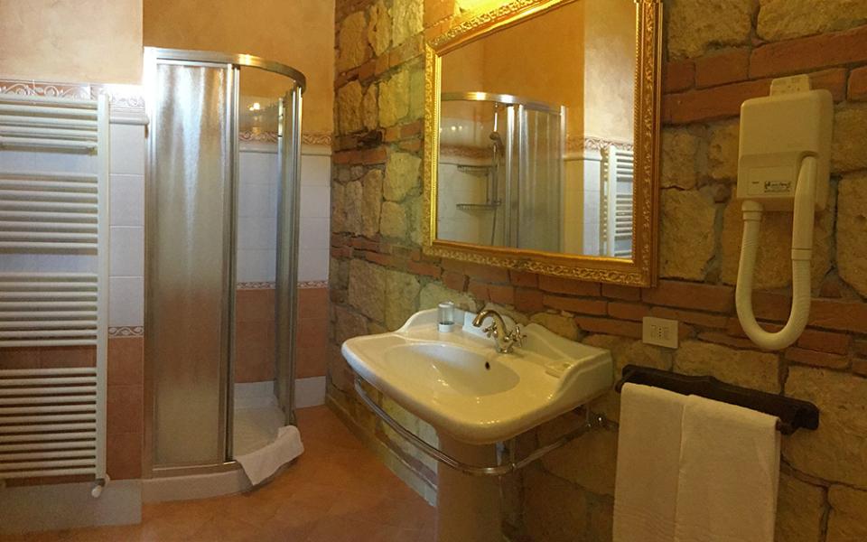 Bagno rustico con doccia, specchio dorato, asciugacapelli e lavabo elegante.