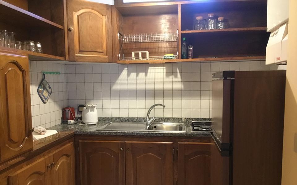 Cucina con mobili in legno, lavello, frigorifero e ripiani aperti.