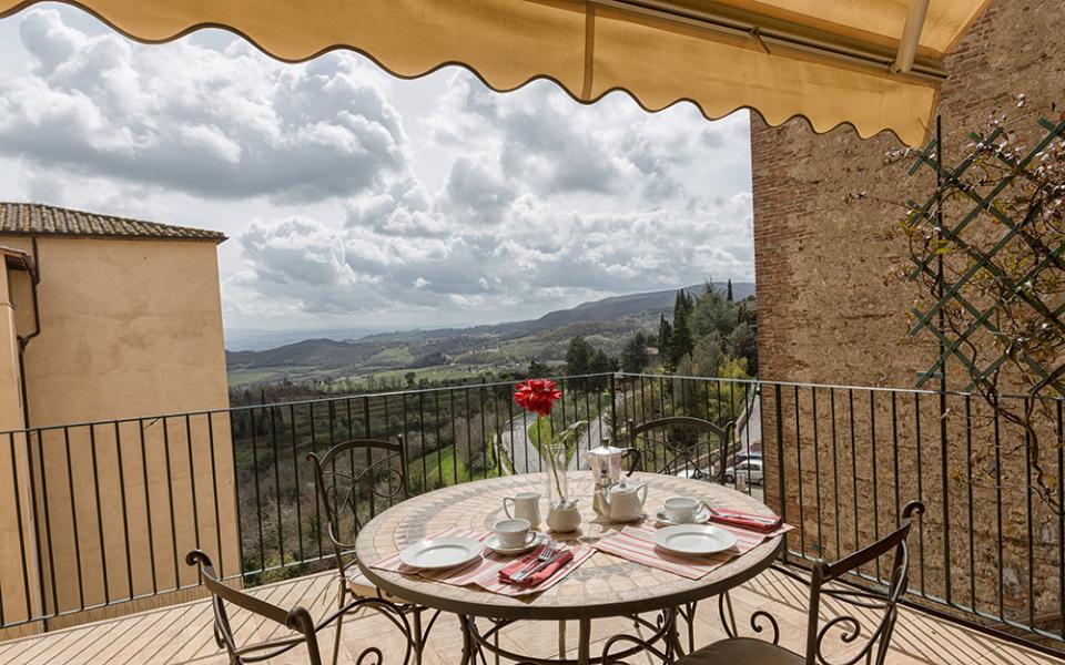 Terrazza con tavolo apparecchiato, vista panoramica su colline e cielo nuvoloso.