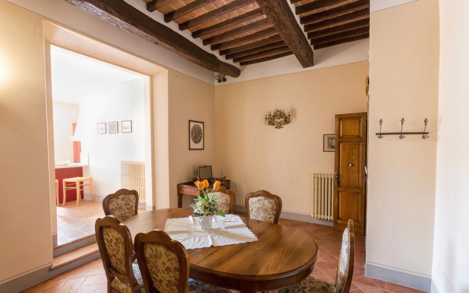 Sala da pranzo con tavolo in legno, sedie imbottite e travi a vista.